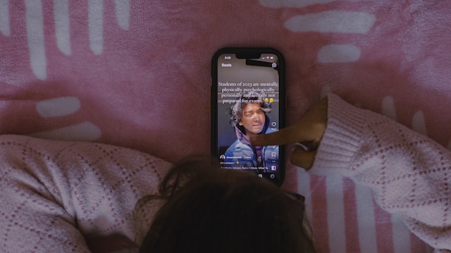 A person in a pink sweater is lying in bed watching an Instagram reel.