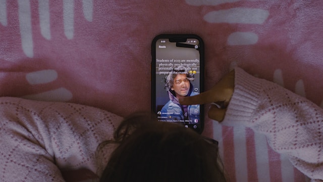 Een persoon in een roze trui ligt in bed naar een Instagram film te kijken.