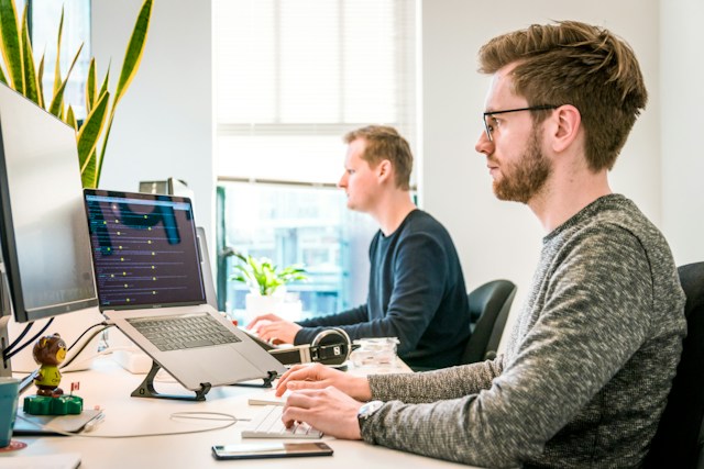 Een man aan dit bureau gebruikt zijn Apple magische toetsenbord naast een collega.