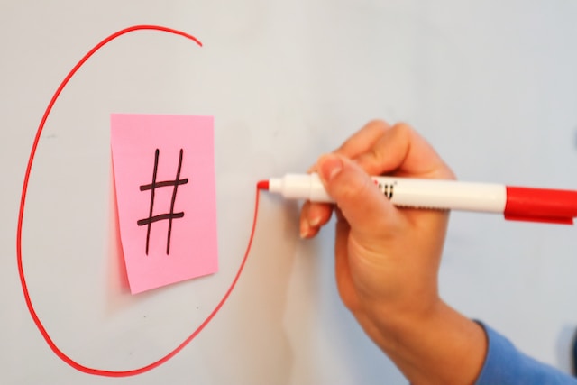 Eine Frau, die mit einem Marker einen Klebezettel mit dem Hashtag-Symbol einkreist.