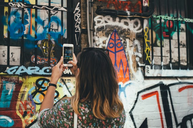 Uma mulher está a tirar uma fotografia de um graffiti na parede com o seu iPhone para publicar em Instagram. 