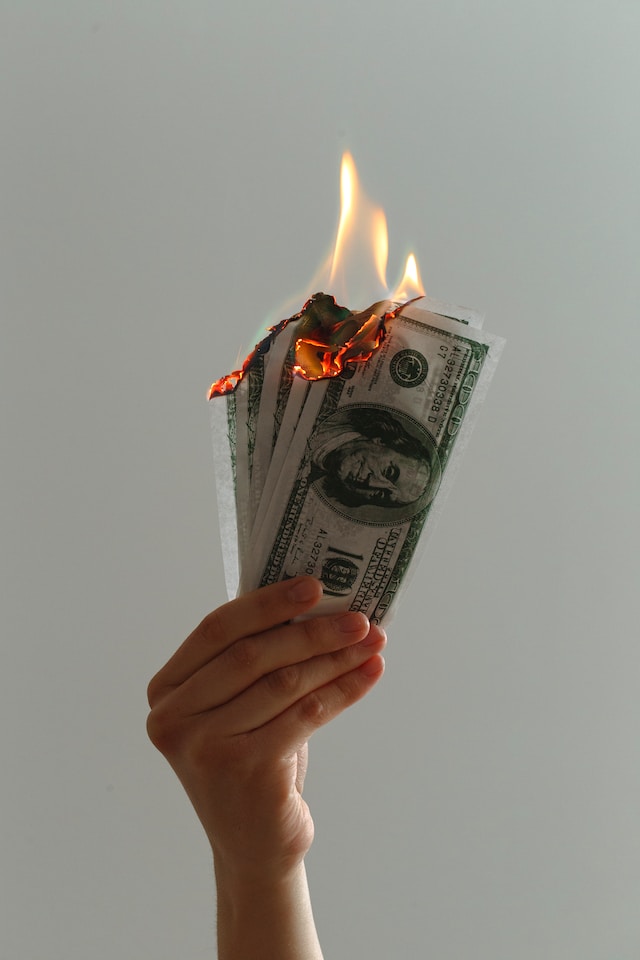 An unseen person holds a few burning US dollar banknotes.