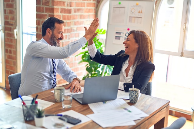 A man and a woman are high-fiving one another for gaining more followers on their business Instagram account. 