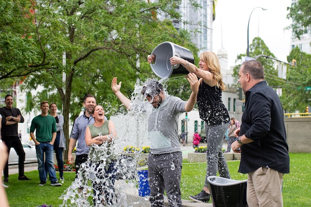 People gathering as a woman pours water over a man’s head as part of the ALS Ice Bucket Challenge.