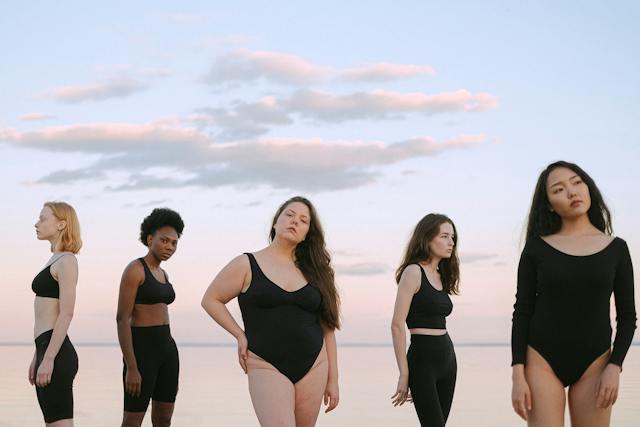Five women with diverse skin tones and body shapes standing next to each other.