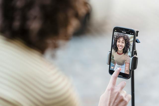 A female influencer smiling as she pushes the record button on her phone to shoot a video.