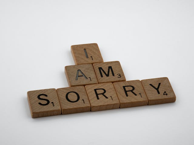 Scrabble letters spelling out “I am sorry” against a white surface.