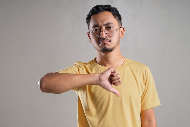 A man frowning while doing a thumbs-down motion.