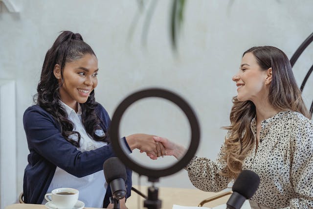 Two female influencers shaking hands after collaborating on a podcast.