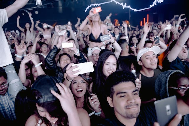A group of excited, loyal fans cheering and taking photos at a concert.
