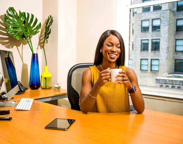 A businesswoman smiling while holding a coffee mug in her office desk.
