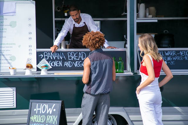 Un vânzător de food truck recomandă clienților săi mâncarea.