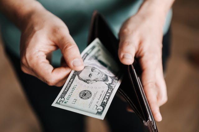 Un hombre saca de su cartera de cuero marrón un billete de cinco dólares.