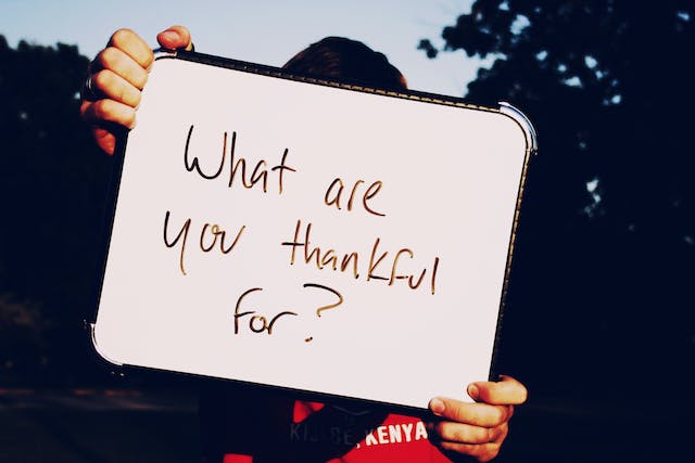 Iemand die een whiteboard omhoog houdt met de vraag "Waar ben je dankbaar voor?" erop geschreven.