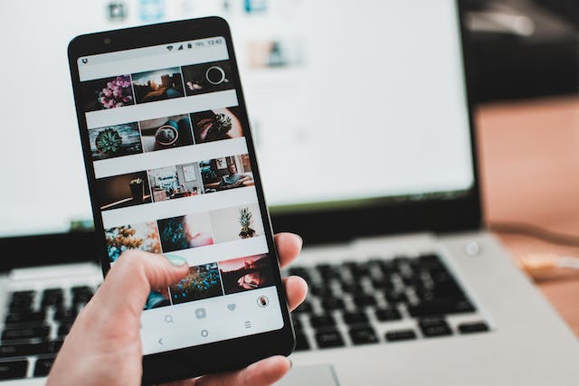 A person is viewing images on the phone in front of a MacBook and planning their next social media post.