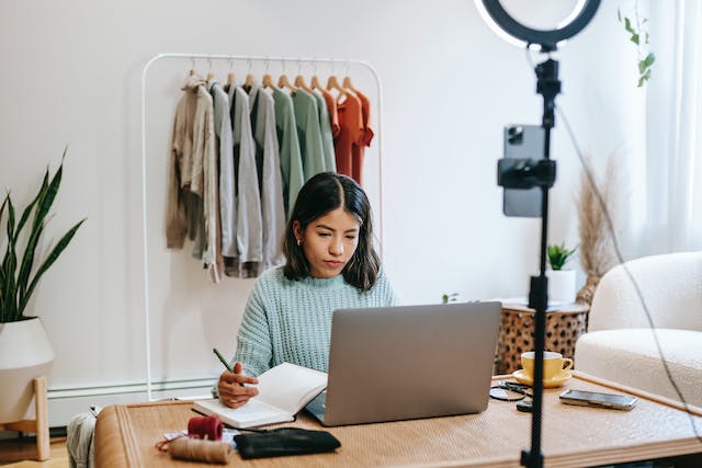 Une femme prend des notes tout en travaillant sur son ordinateur portable.