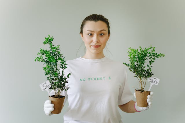A woman holding newly potted plants while wearing a shirt that says, “No Planet B.”