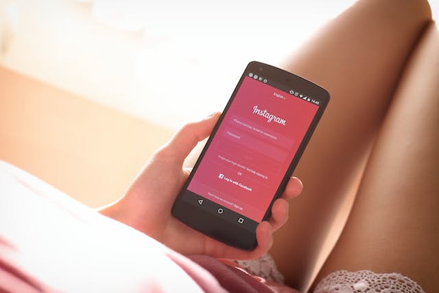 An image of a woman's hand holding a phone with the Instagram login page opened.