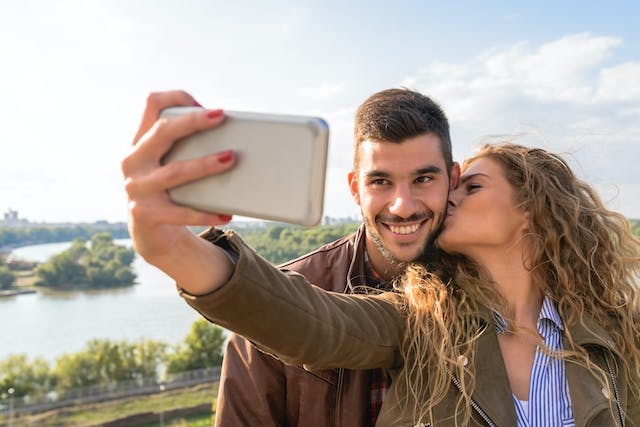 Eine Frau küsst einen Mann auf die Wange, während sie ein Selfie macht.