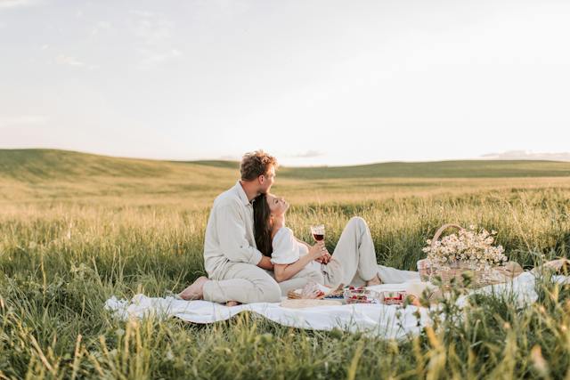 Un bărbat și o femeie care se bucură de un picnic romantic pe un câmp cu iarbă.