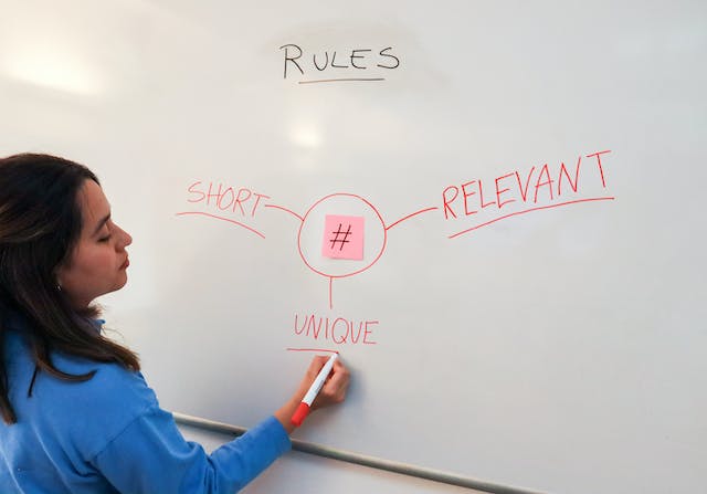 A woman writing the words “short,” “relevant,” and “unique” on a whiteboard to describe the hashtag symbol.