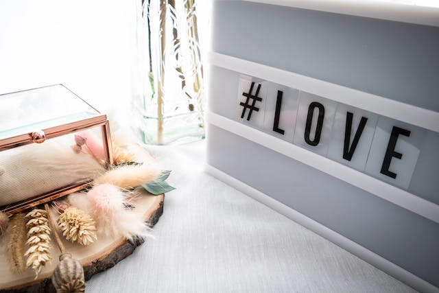  Een juwelendoosje en gedroogde bloemen naast een letterbord met de tag "#LOVE".