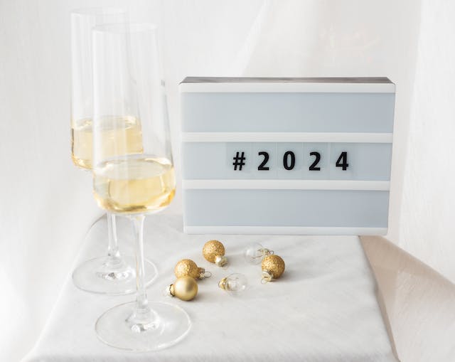 A sign saying #2024 beside two glasses and Christmas decorations on a table.