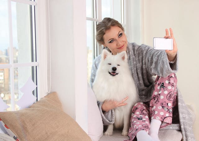 Eine Frau lächelt, während sie ein Selfie mit ihrem Hund macht.