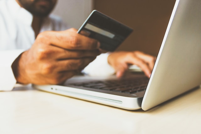 Un uomo con una carta di credito in mano davanti al suo computer portatile sta valutando se acquistare i follower di Instagram . 