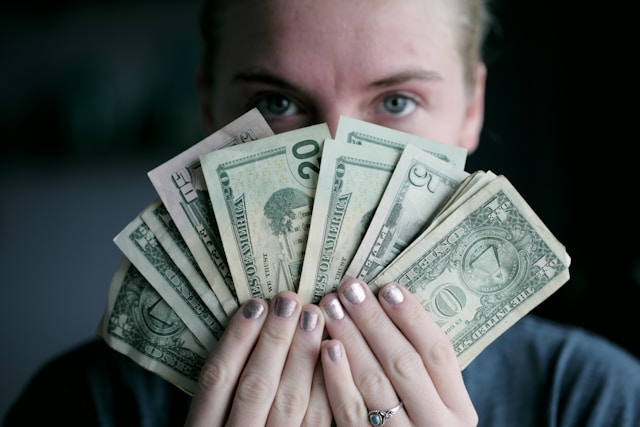 Een vrouw die de onderste helft van haar gezicht bedekt met een waaier van dollarbiljetten.