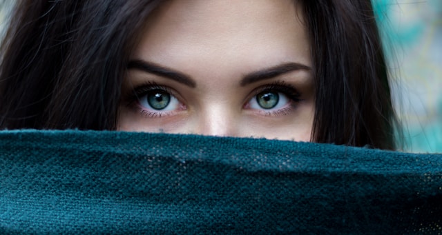 Een vrouw kijkt naar de camera terwijl ze de onderste helft van haar gezicht bedekt met een doek.