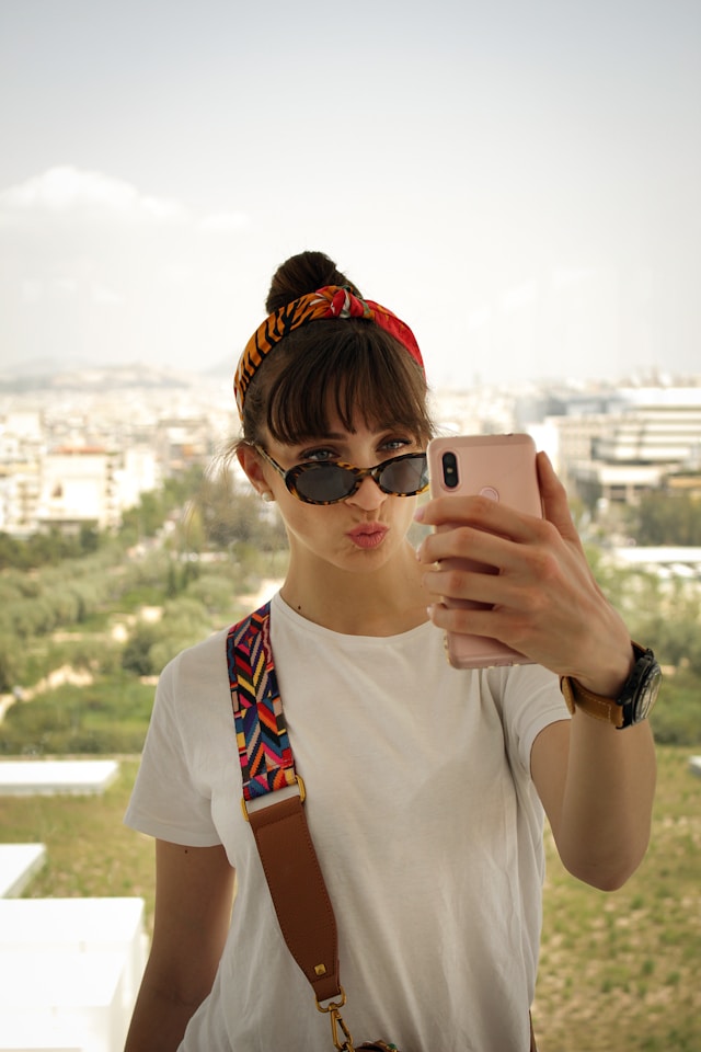 Une femme portant un bandana rouge et une chemise blanche prend un selfie. 