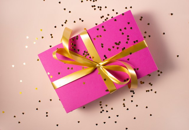 Una caja de regalo rosa atada con una cinta dorada con confeti dorado alrededor.