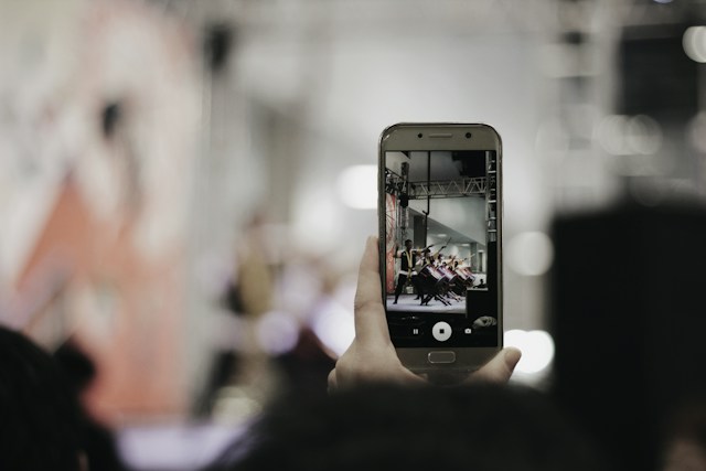 Iemand die zijn telefoon omhoog houdt om een video te maken van een optreden om later te publiceren op Instagram Reels.