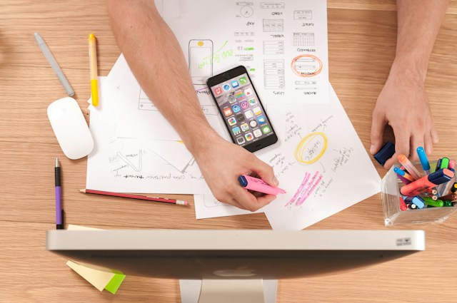 eine Person, die mit einem Stift und einem Mobiltelefon auf Papier schreibt