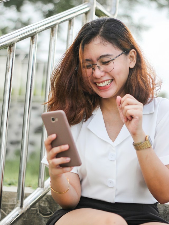 一個穿著白襯衫、戴著眼鏡的女孩一邊看手機一邊表達幸福。 