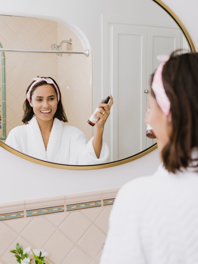 Une femme souriante vaporisant un produit de soin sur son visage.