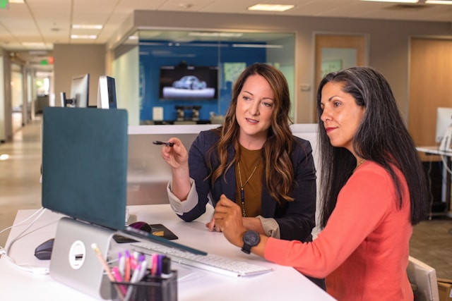 Twee vrouwen kijken naar hun computerscherm terwijl ze discussiëren.