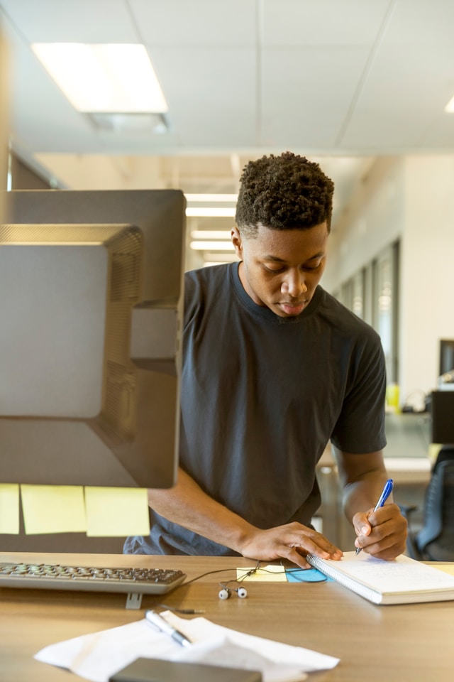 A man in a black shirt is writing in a notebook. 