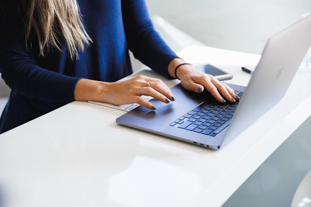 Une femme en chemise bleue tape sur son MacBook Pro.