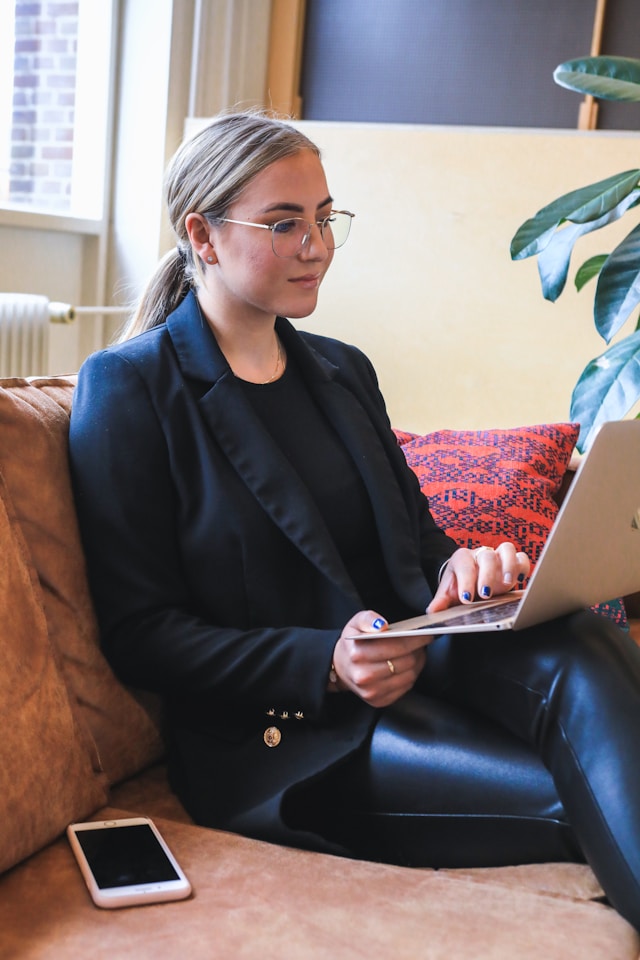 Une femme en blazer noir et lunettes tape sur son ordinateur portable.