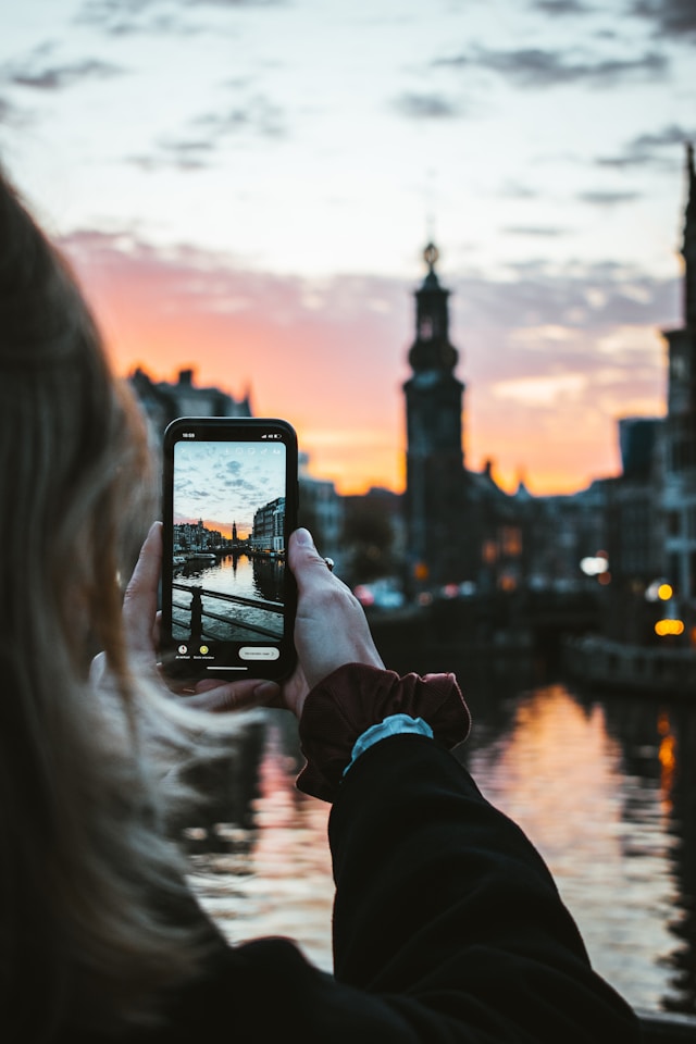 Een vrouw neemt een foto van een gebouw tijdens zonsondergang. 