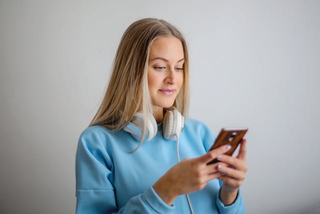 O femeie cu o cască la gât își folosește telefonul mobil.