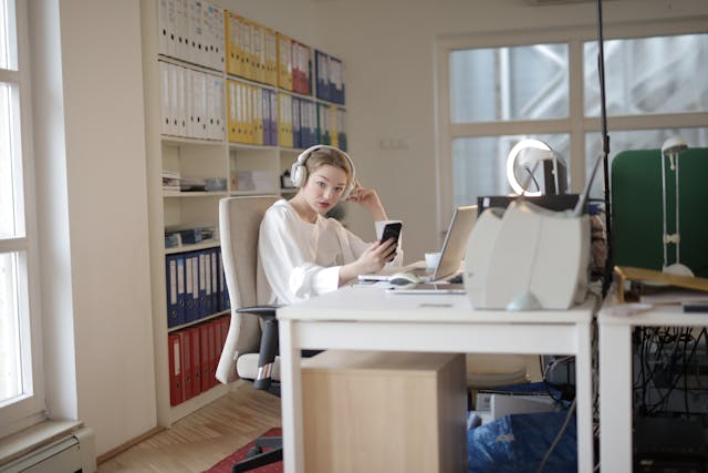 A woman with earphones holds a phone while she stares at something.