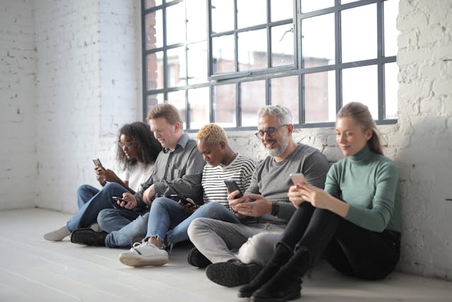 Un gruppo di persone sedute in fila mentre usano il cellulare.