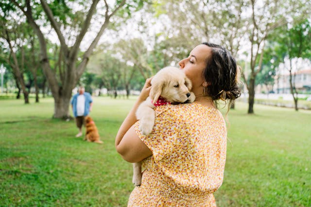 A woman carrying a cute puppy in the middle of a park.