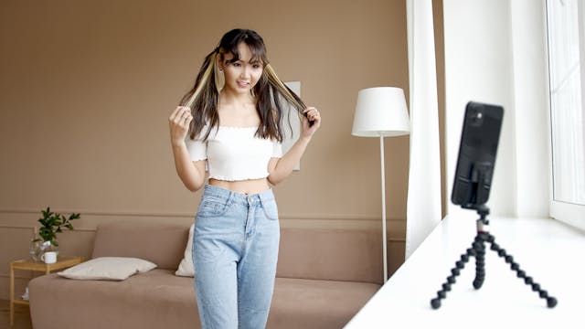 A woman standing in front of a phone and tripod to record a video.