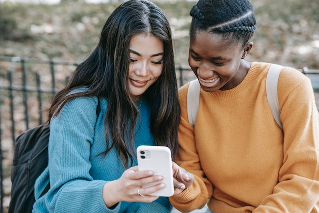 Twee vrouwen glimlachen terwijl ze iets bekijken op een smartphone.