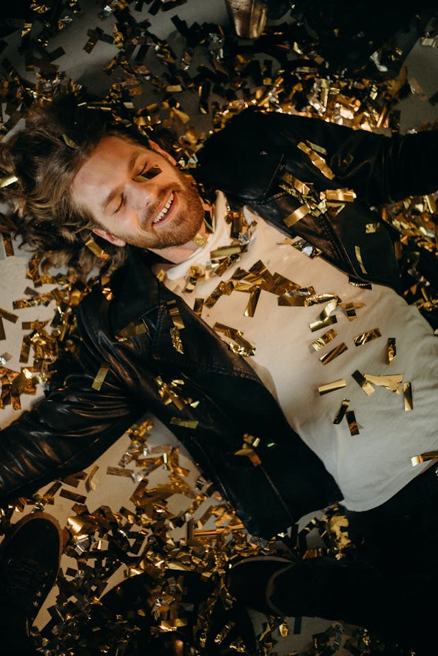 Um homem deitado de olhos fechados com confettis à sua volta numa festa.