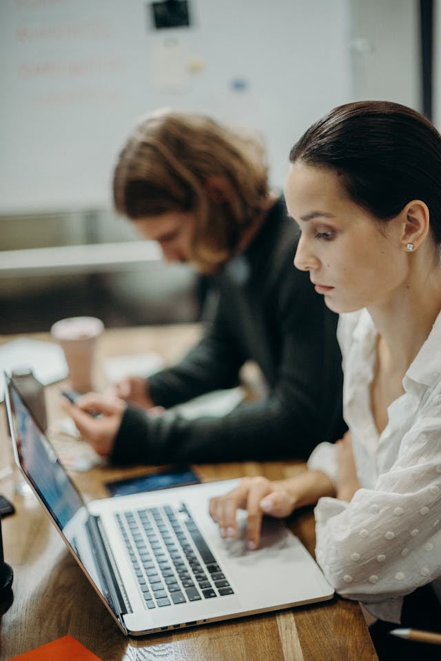 Una donna in camicia bianca sta usando il suo computer portatile. 